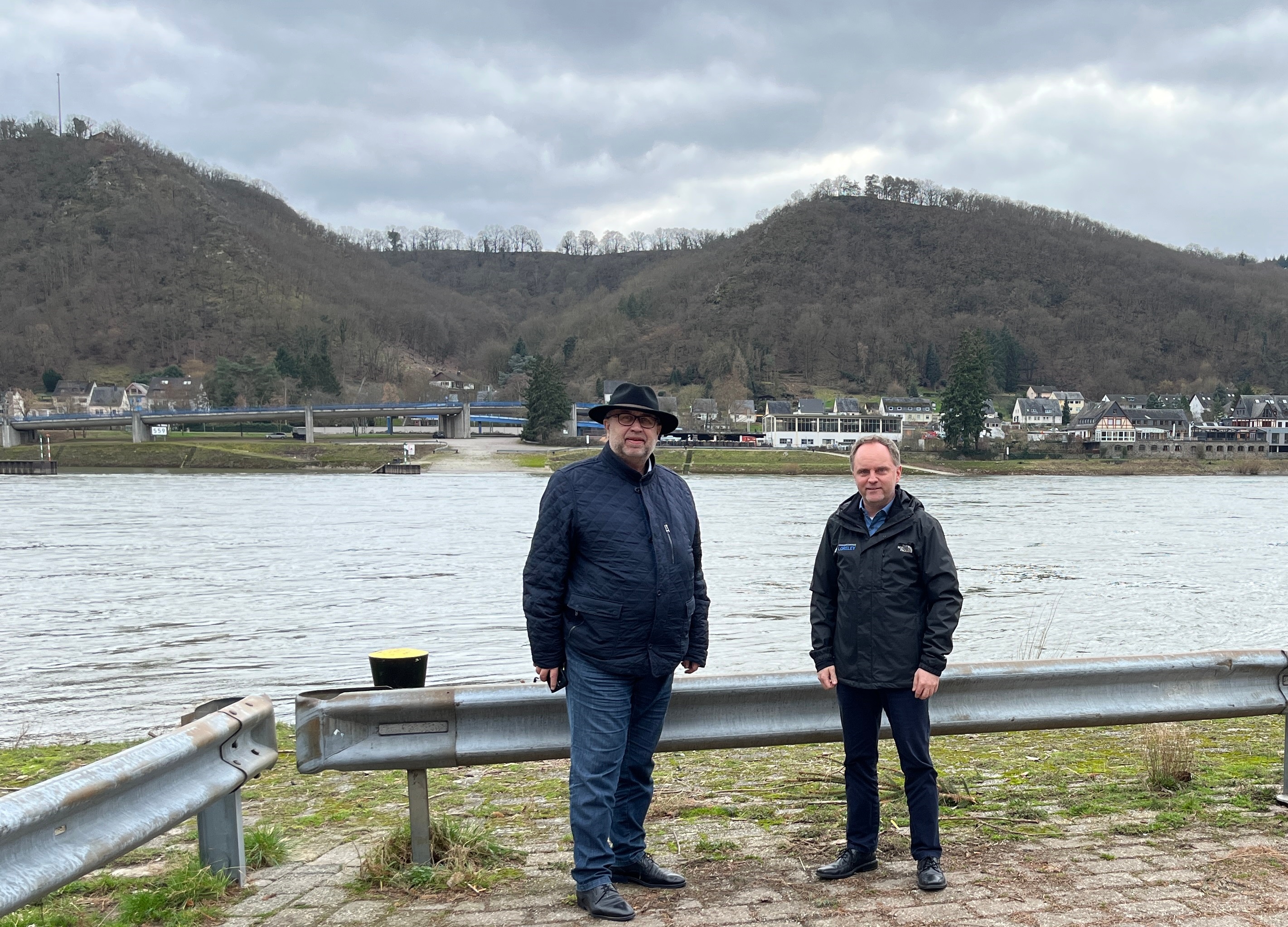 Bürgermeister der Verbandsgemeinde Loreley, Mike Weiland (rechts), und der Regionalgeschäftsführer der IHK Koblenz, Richard Hover (links), am geplanten Standort der Mittelrheinbrücke in St. Goarshausen-Wellmich.