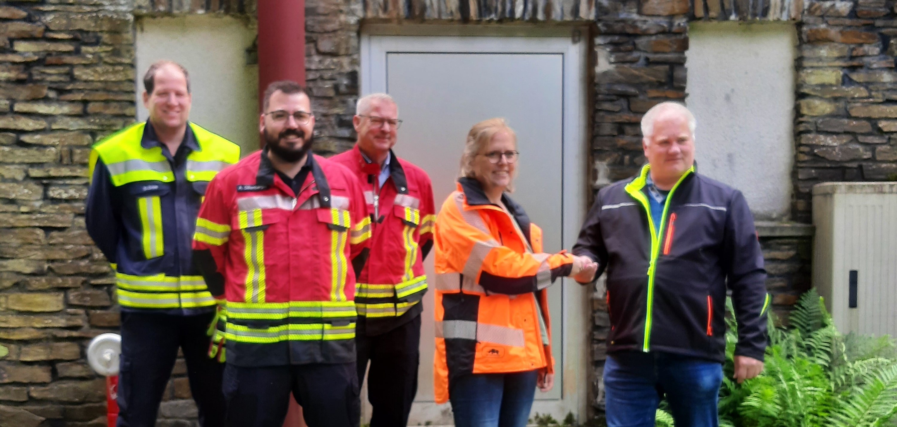 Werkleiter Michael Krämer übergibt den Schlüssel des Hochbehälters Kaub an Forstamtsleiterin Susanne Gühne im Beisein von Kaubs Wehrführer Sebastian Gros, dem stellvertretenden Wehrleiter Andre Dillenberger und Wehrleiter Jörg Preißmann. Die Übergabe erfolgt vor dem Hochbehälter und die Feuerwehrleute sind in Feuerwehrkleidung gekleidet.