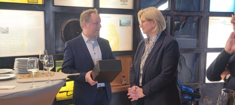 Bürgermeister Mike Weiland überreicht eine schwarze Box, in der sich eine Flasche Wein befindet, an Saarlands Ministerpräsidentin Anke Rehlinger.