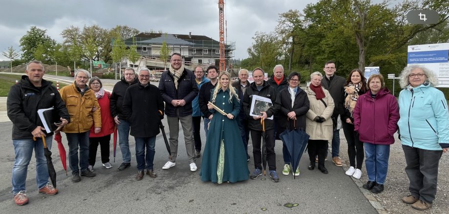Gruppenfoto Tag der Städtebauförderung 2024 18 Personen stehen am Eingang zum Kultur- und Landschaftspark für ein Gruppenfoto zusammen. Das Wetter ist leicht bewölkt und im Hintergrund ist das ehemalige Turner- und Jugendheim mit einem Baukran zu sehen.