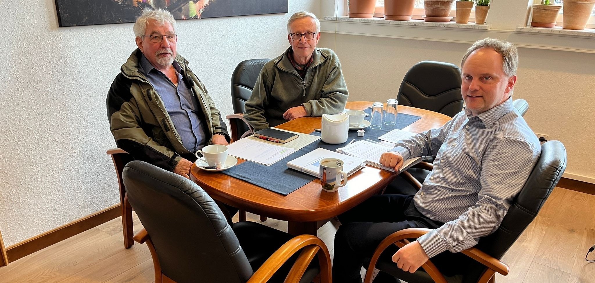 Zwei männliche Vertreter der Bürgerinitiative und Bürgermeister Mike Weiland sitzen an einem Besprechungstisch. Auf dem Tisch sind Kaffeetassen und verschiedene Unterlagen zu sehen.
