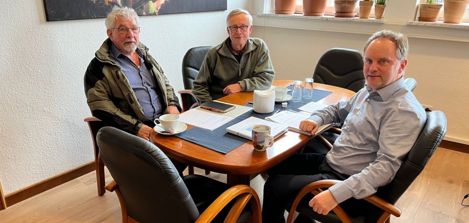 BI Braubach lebenswerter E.V. Zwei männliche Vertreter der Bürgerinitiative und Bürgermeister Mike Weiland sitzen an einem Besprechungstisch. Auf dem Tisch sind Kaffeetassen und verschiedene Unterlagen zu sehen.