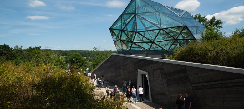 Gläserner Fels der neuen Mythoshalle bei Sonnenschein und blauem Himmel
