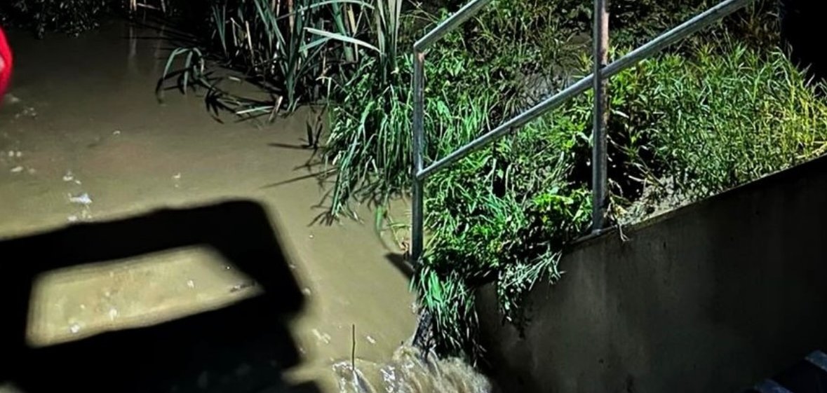 Das Bild zeigt einen über die Ufer getretenen Bach vor einem Rechen einer Bachunterführung