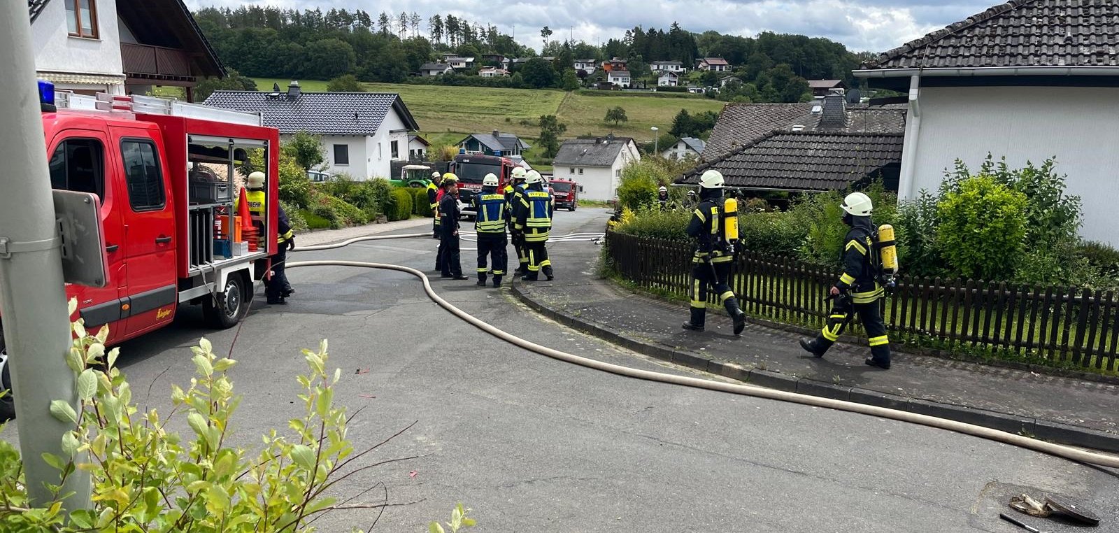 Das Bild zeigt ein Feuerwehrfahrzeug vor einem Gebäude und zwei Feuerwehrmänner nach dem Einsatz